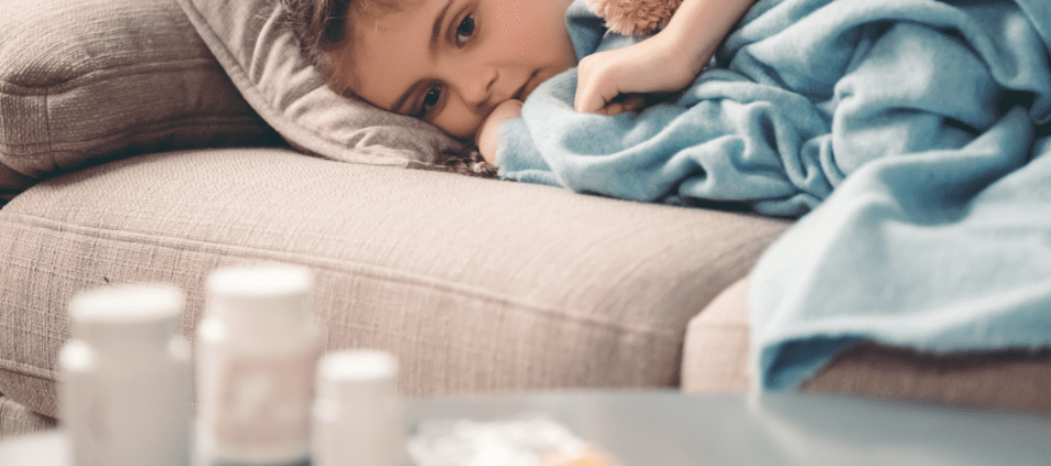Sick child with blanket resting on sofa near medicine