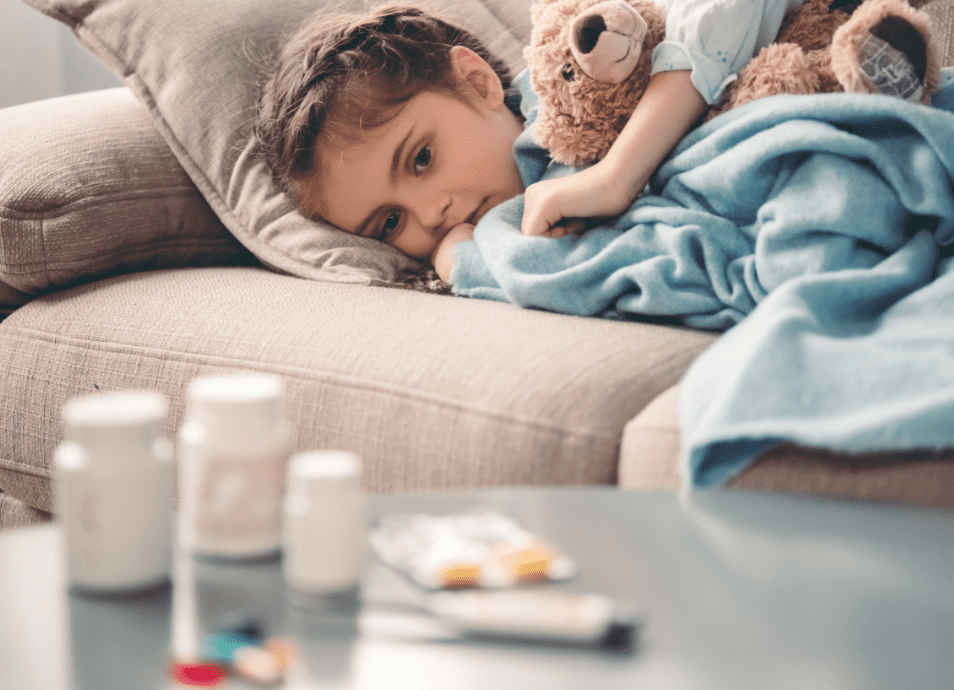 Sick child with blanket resting on sofa near medicine