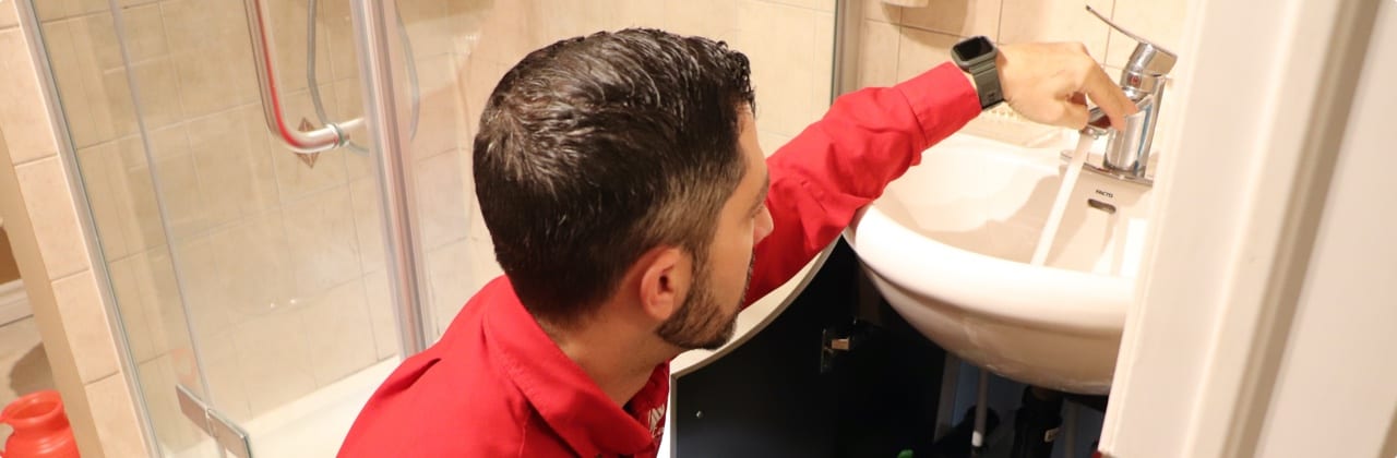 Atlas care worker in red uniform fixing faucet for bathroom sink